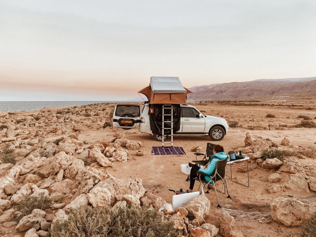 Woman sat amongst rocks on a camp chair in front of a roof tent at Fins, Oman